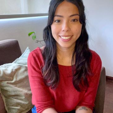 Young woman in a red top smiling at the camera indoors.