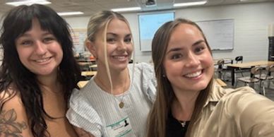 Three young women smiling and posing for a selfie in a classroom.