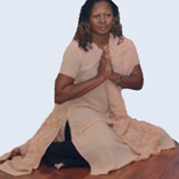 Woman kneeling on floor with hands in prayer pose, wearing light pink dress.