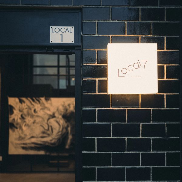 Lighted sign reading 'Local 7' on a black brick wall next to a door.