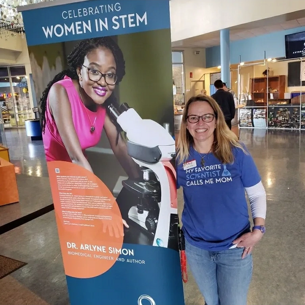 Women scientist standing next to banner stating "Celebrating Women in STEM."