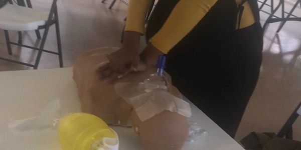Person practicing CPR on a training manikin on a table.