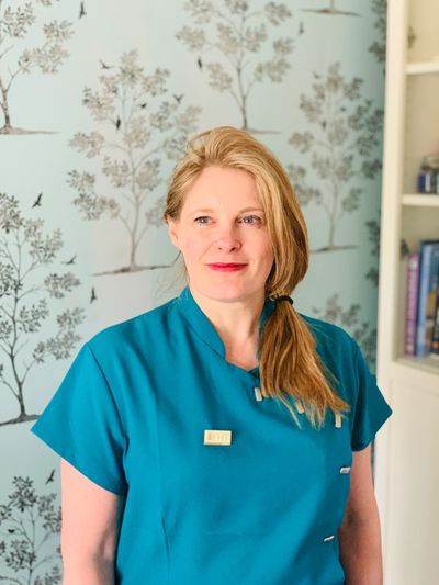 A woman in a teal medical uniform with light brown hair tied in a ponytail.