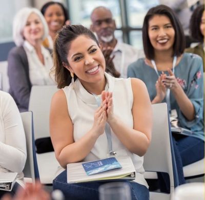 Smiling woman clapping at an event with diverse audience.