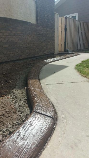 Curved concrete border designed to look like wood beside a sidewalk.