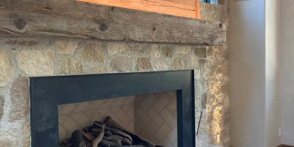 Rustic stone fireplace with stacked firewood and wooden mantel.