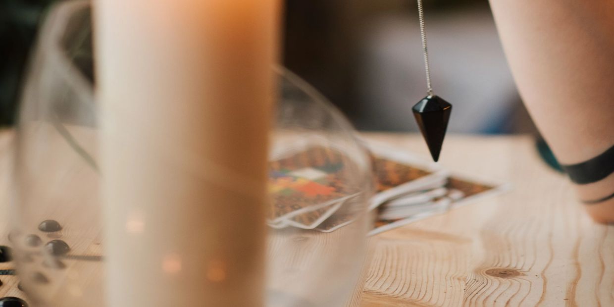 Pendulum swinging over tarot cards on a wooden table with a candle.