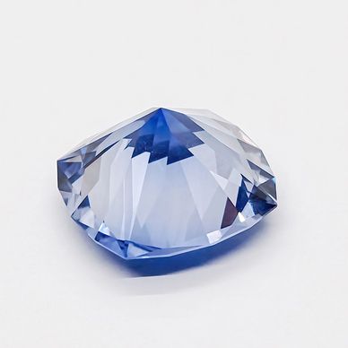 A sparkling blue faceted gemstone on a white surface.