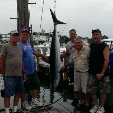 Five men posing with a large caught fish at a dock.