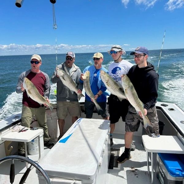 Group of five men holding large fish on a boat at sea.