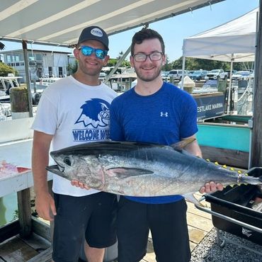 Two men holding a large fish on a dock.