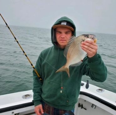Young man holding a freshly caught fish on a boat.