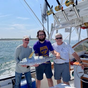Three men on a boat holding a large fish.
