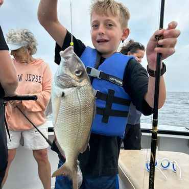 Smiling boy holding a large fish on a boat.