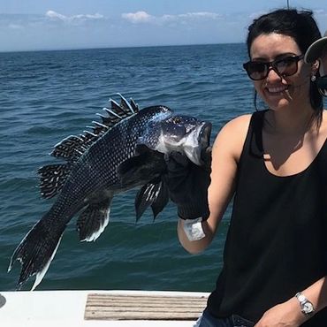 Person holding a large black sea fish while on a boat.