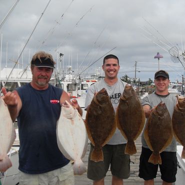 Three men holding flatfish on a dock.