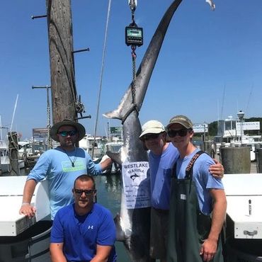 Four men posing with a large caught fish on a dock.