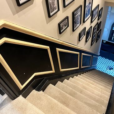 Carpeted staircase with black and gold paneled walls and framed photos.