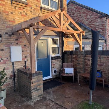 A brick house entrance with a wooden porch frame and outdoor seating area.