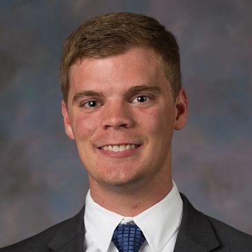 Young man in a suit smiling against a blurred background.
