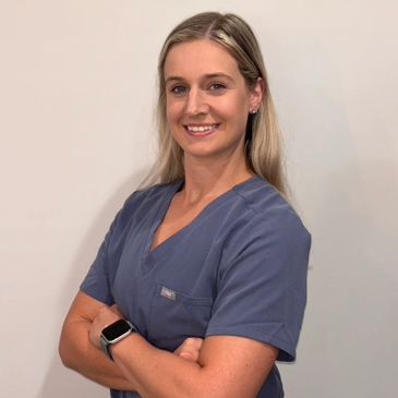 A confident woman in blue medical scrubs smiling with arms crossed.
