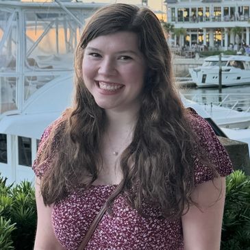 Smiling young woman in a floral dress by a marina at sunset.