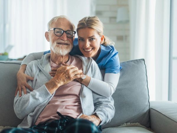 Elderly man and caregiver sharing a happy moment on the couch.