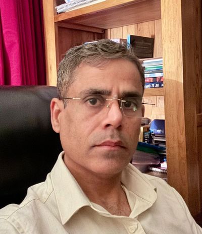 Man wearing glasses sitting in an office chair with bookshelves behind.