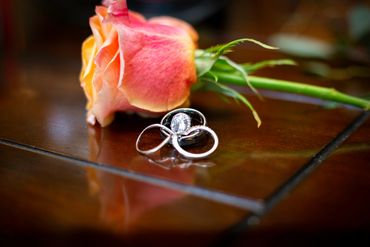 wedding bands on a table in front of a pink tinged with yellow rose 