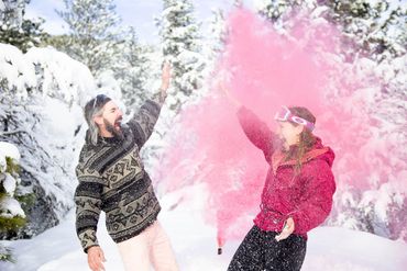 Newly engaged couple doing a high five in the snow with a pink colored smoke bomb 