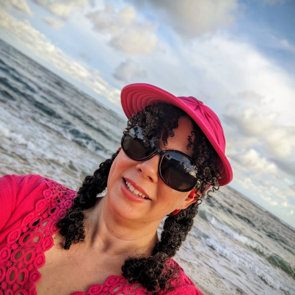 Woman in pink hat and sunglasses by the ocean.