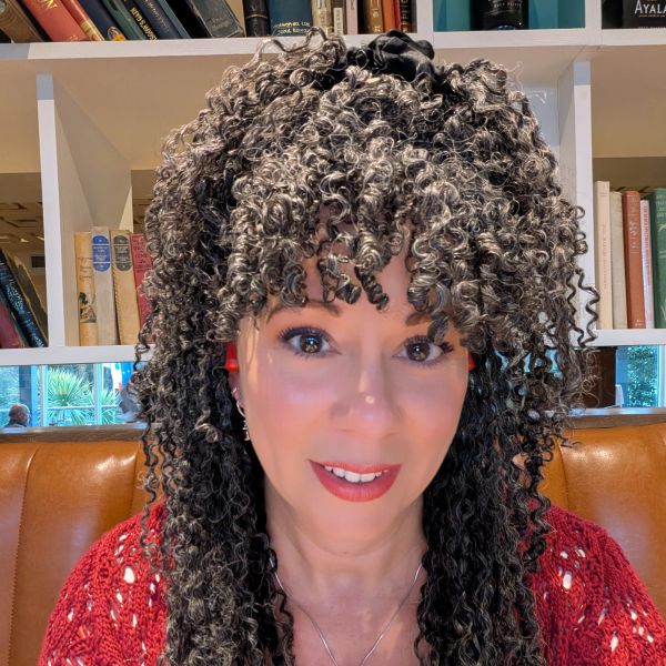 Woman with curly hair and red sweater smiling indoors.