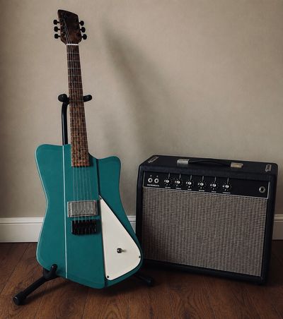 Teal electric guitar with amplifier on wooden floor.