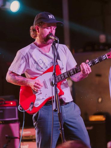 Man playing red electric guitar and singing on stage.