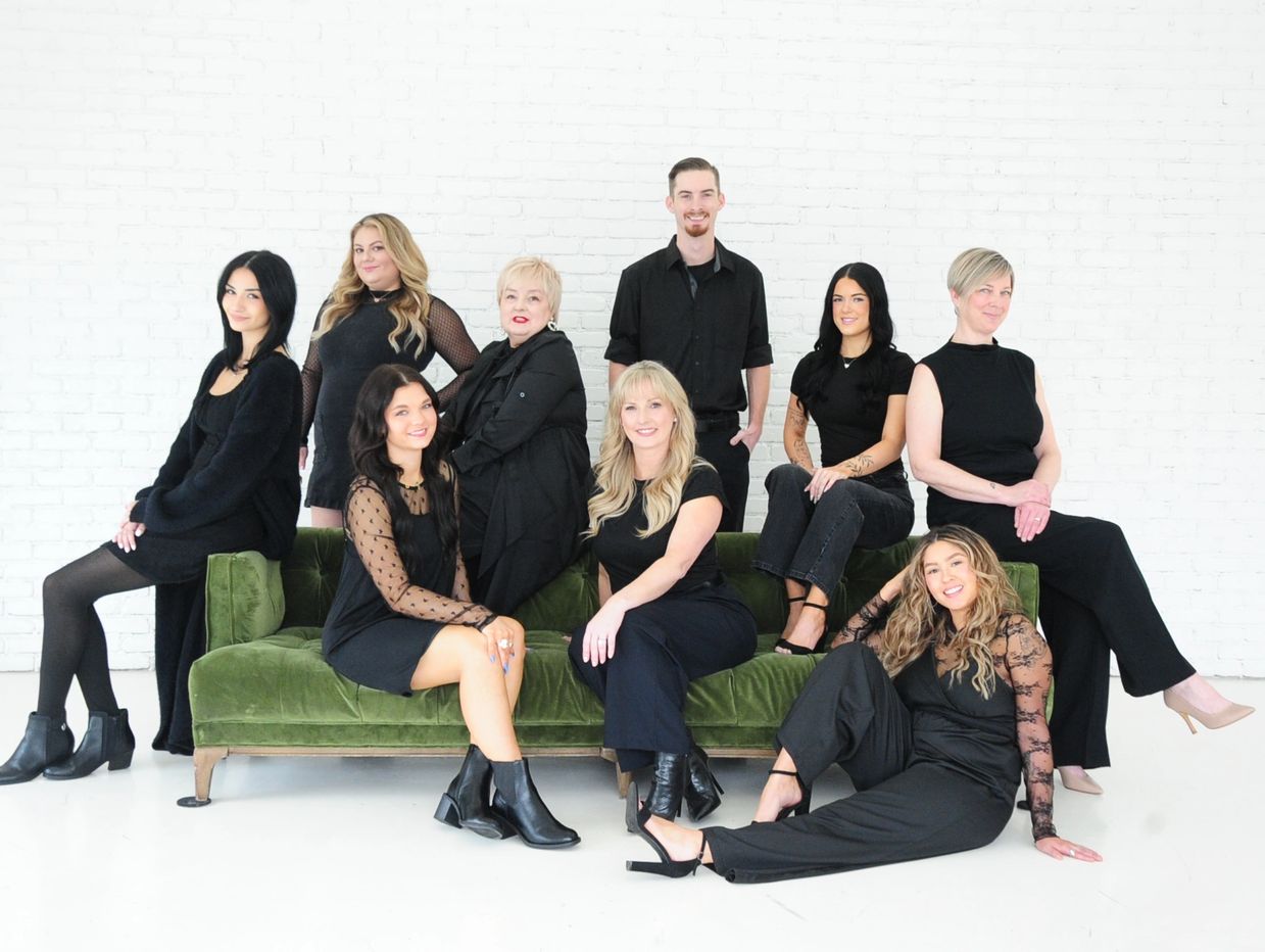 A group of ten people dressed in black posing around a green velvet sofa against a white brick wall.