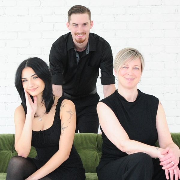 Three people dressed in black posing on and behind a green velvet couch.