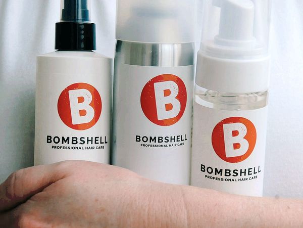 Three Bombshell Professional Hair Care bottles with a hand in front.