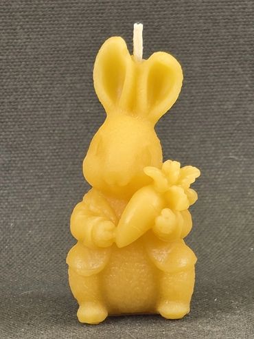 Yellow bunny-shaped candle holding a carrot against a gray background.