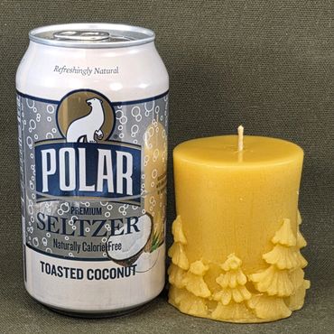 Can of Polar Premium Spitzer Toasted Coconut next to a yellow candle with tree designs.