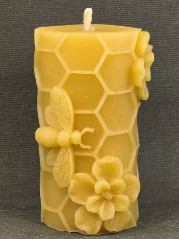 A yellow candle with bee and flower designs on a honeycomb pattern.