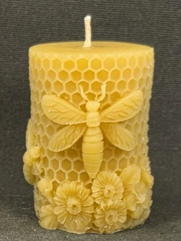 Decorative beeswax candle with bee and flower designs.