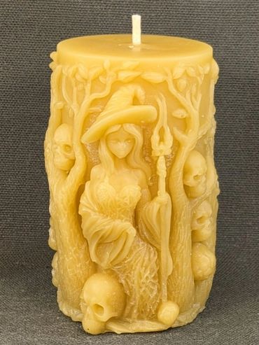 Intricately carved candle featuring a witch surrounded by skulls and trees.
