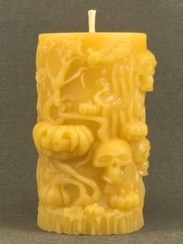 Yellow candle with intricate Halloween-themed carvings of skulls and pumpkins.