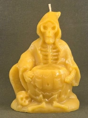 Yellow candle shaped like a skeleton in a hooded cloak with a pumpkin and skull.