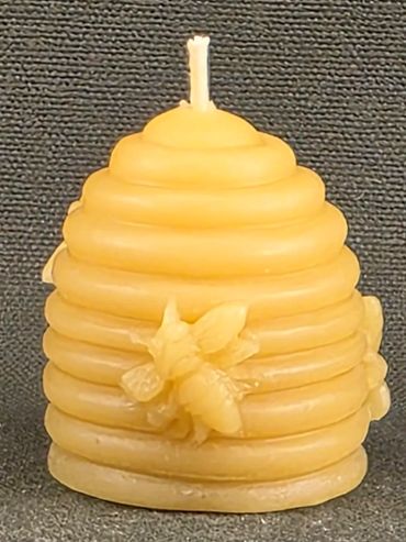 Beehive-shaped yellow candle with a bee decoration.