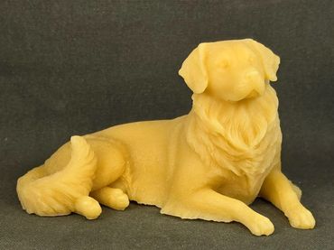 A detailed yellow sculpture of a dog lying down on a dark surface.