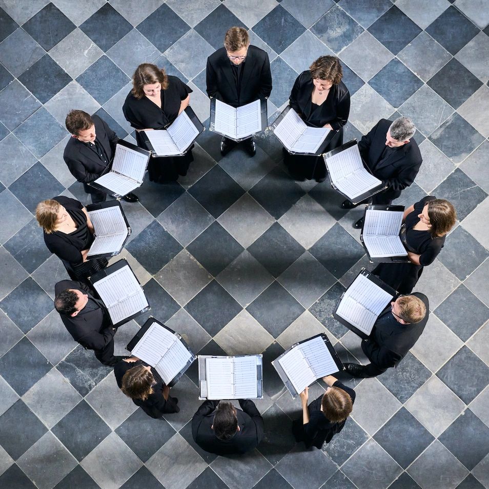 Choir group standing in a heart shape while holding music sheets.