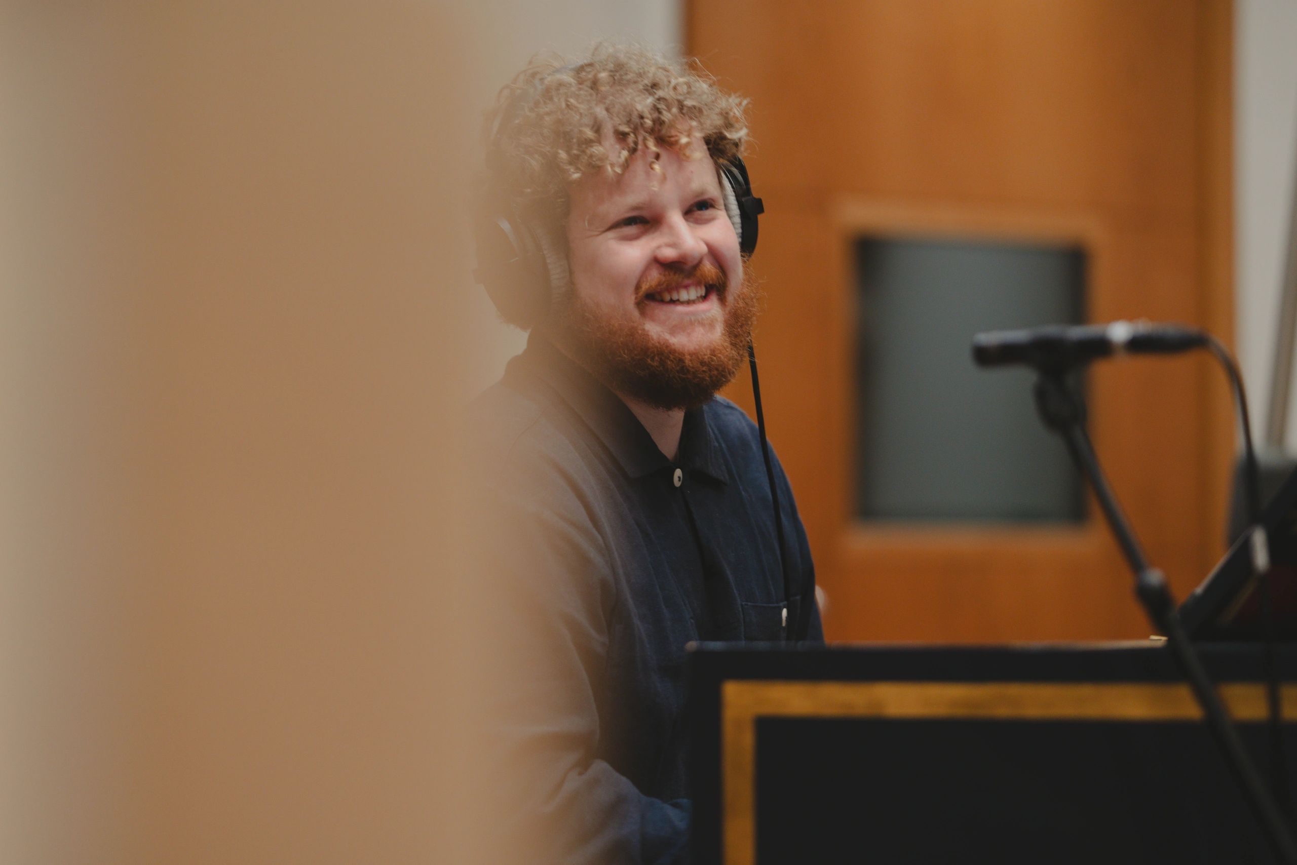 Man with curly hair and headphones smiling in a studio.