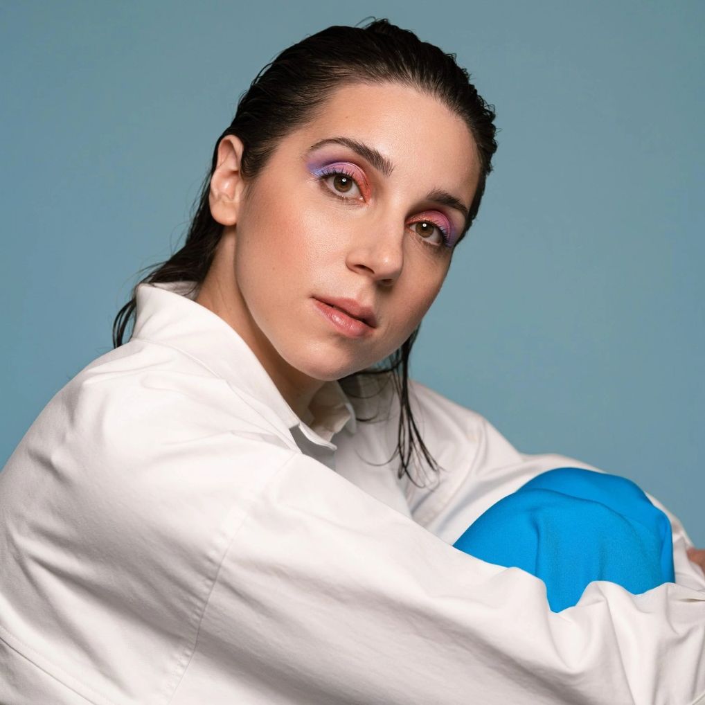 Young woman with wet hair wearing colorful eye makeup and a white shirt.