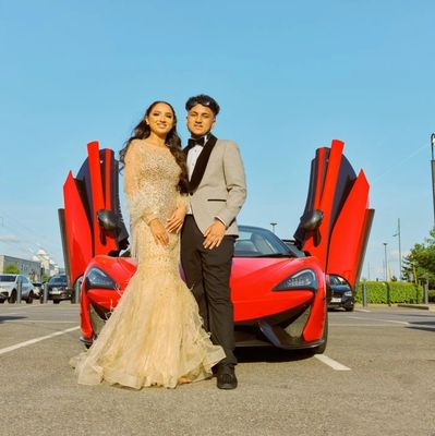 Elegantly dressed couple posing in front of a red sports car with open doors.